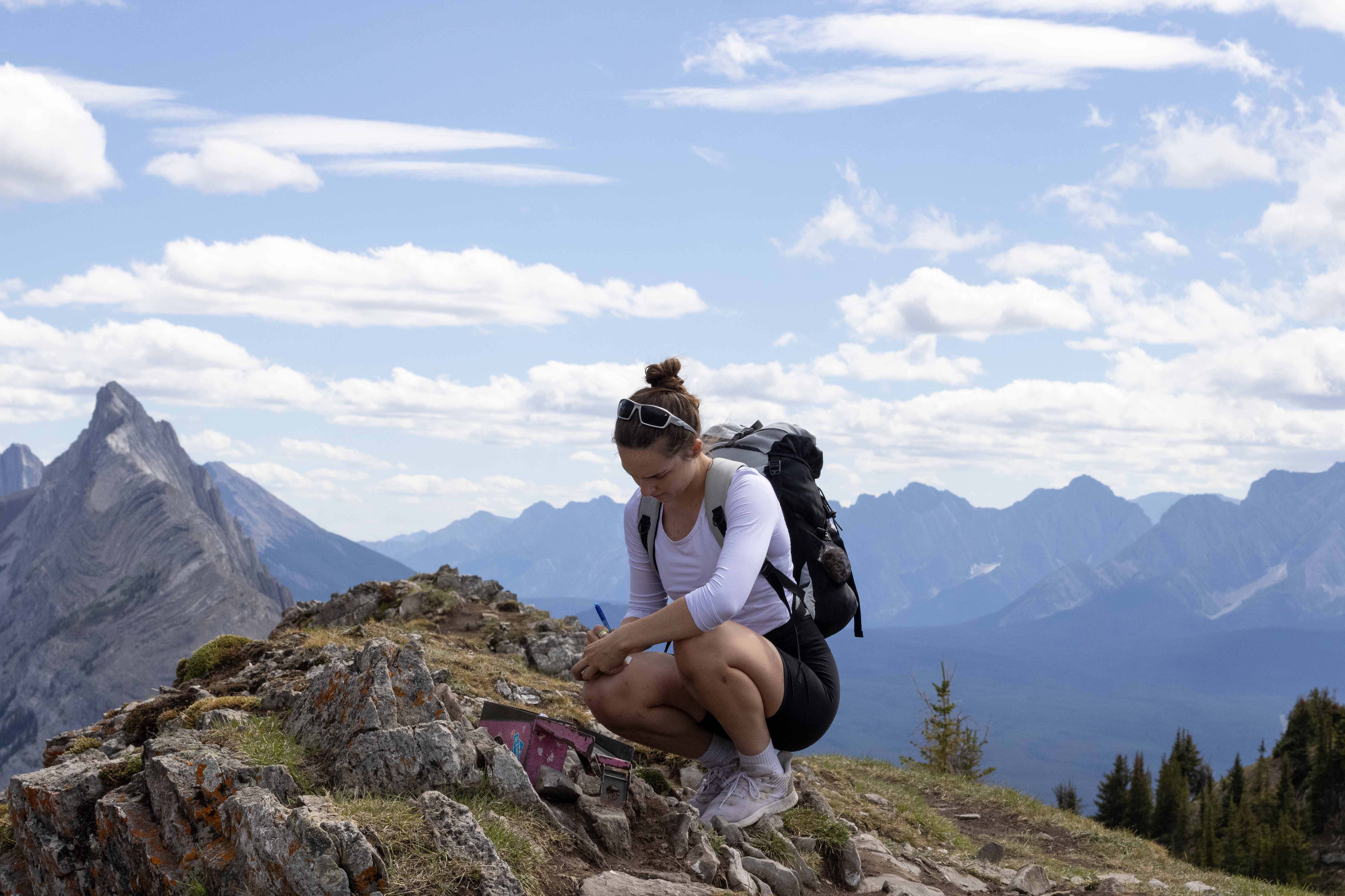 Photo of model summiting a mountain writing a note in an amunition box